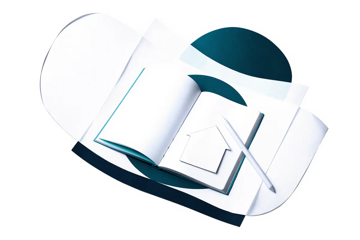 Open paper notebook with a paper pencil and a small paper house resting on it